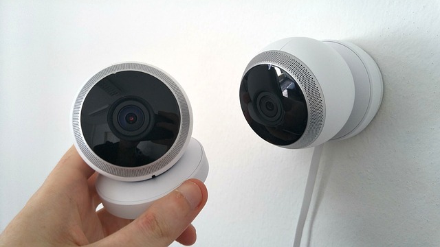 A hand holding one Security camera near another plugged on the wall